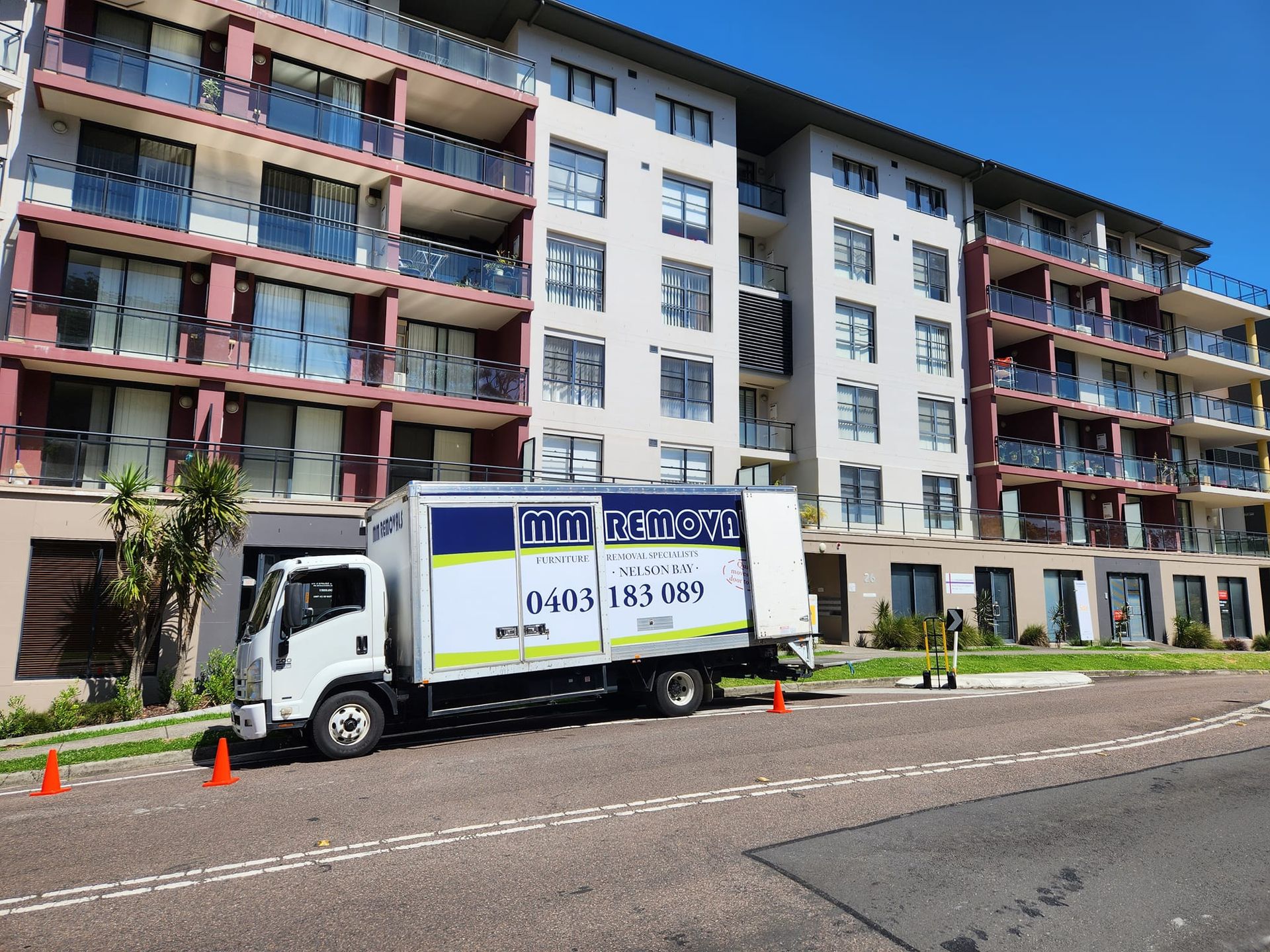 White Truck with Green Signage Parked Outdoors Under a Blue Sky — MM Removals In Shoal Bay, NSW