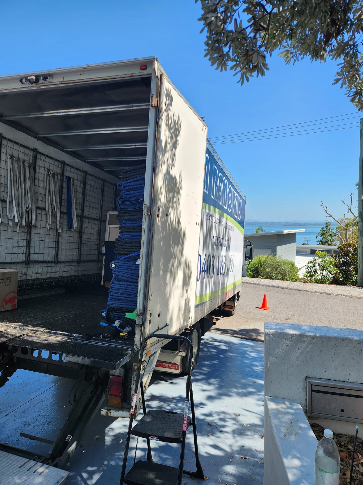 Moving Truck Parked on A Sunlit Driveway Beside a House — MM Removals In Nelson Bay, NSW