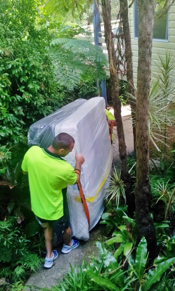 Person in neon green shirt moving a wrapped appliance through a narrow garden path — MM Removals In Nelson Bay, NSW