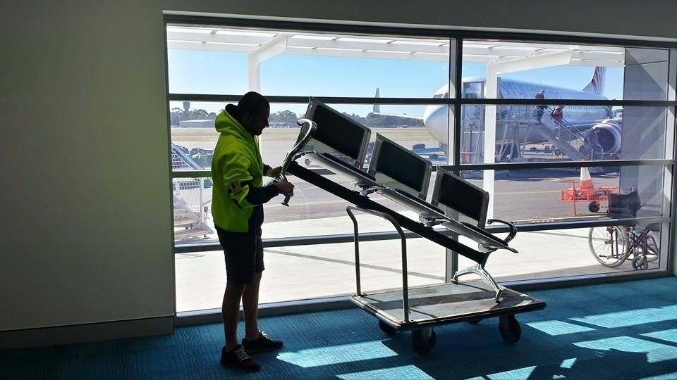 Worker in A Neon Jacket Operating a Tilted Luggage Cart Beside Large Windows at An Airport — MM Removals In Nelson Bay, NSW