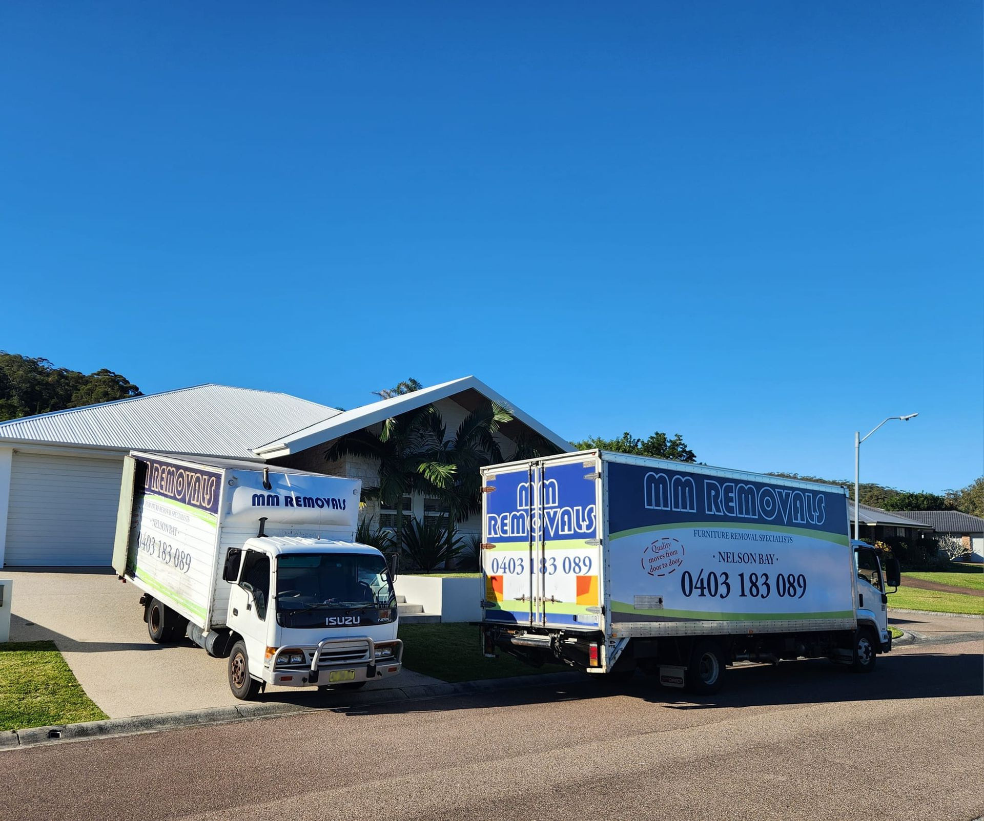Two White Delivery Trucks Parked Outside a Small Building — MM Removals In Nelson Bay, NSW