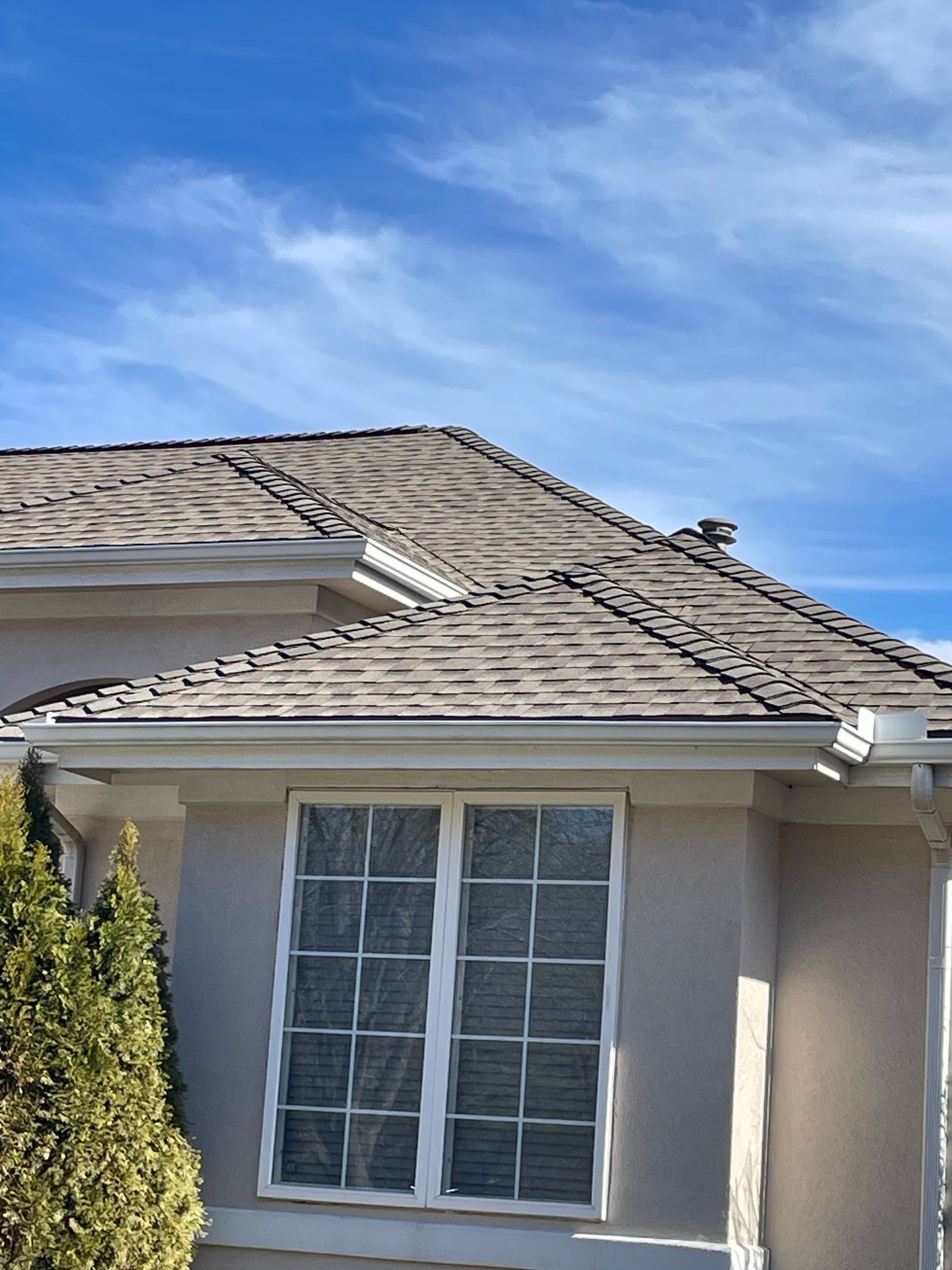 House exterior with beige stucco, white-trimmed windows, and a gray shingled roof under a blue sky