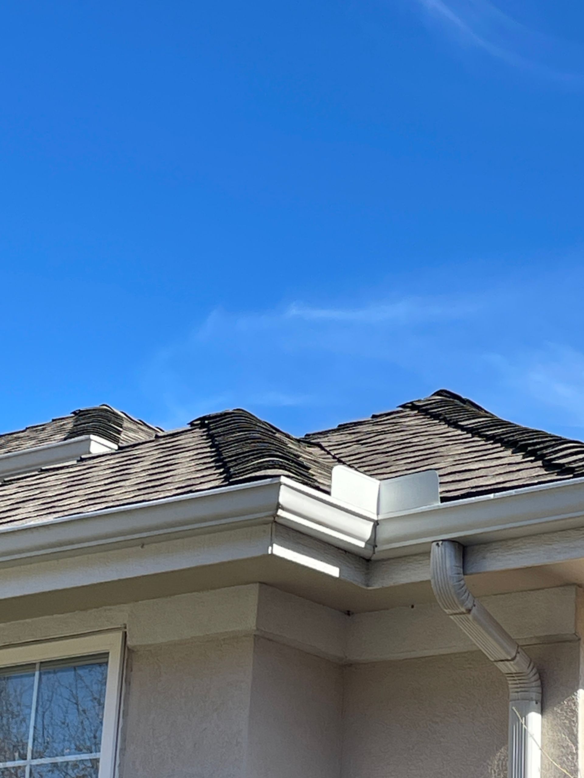 Damaged roof shingles on a beige house under a clear blue sky