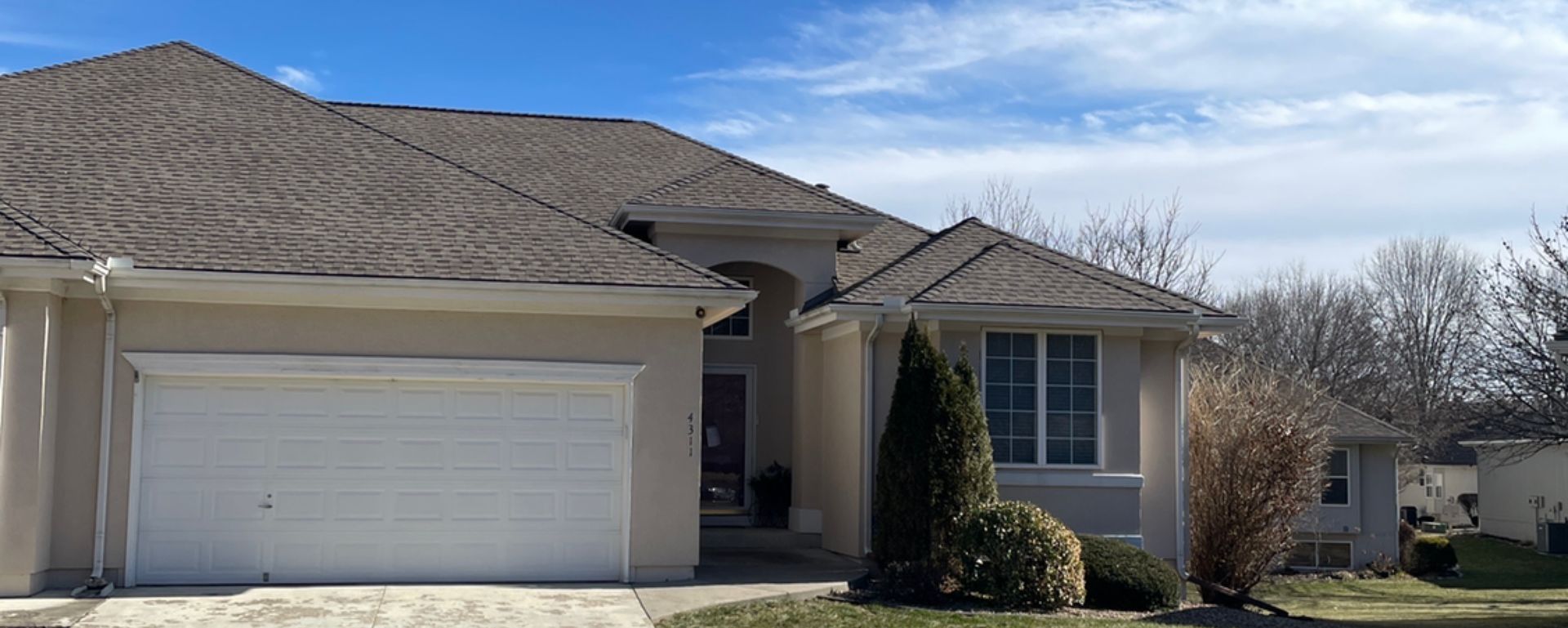 Suburban house with beige siding, white garage door, and small front porch in winter landscape