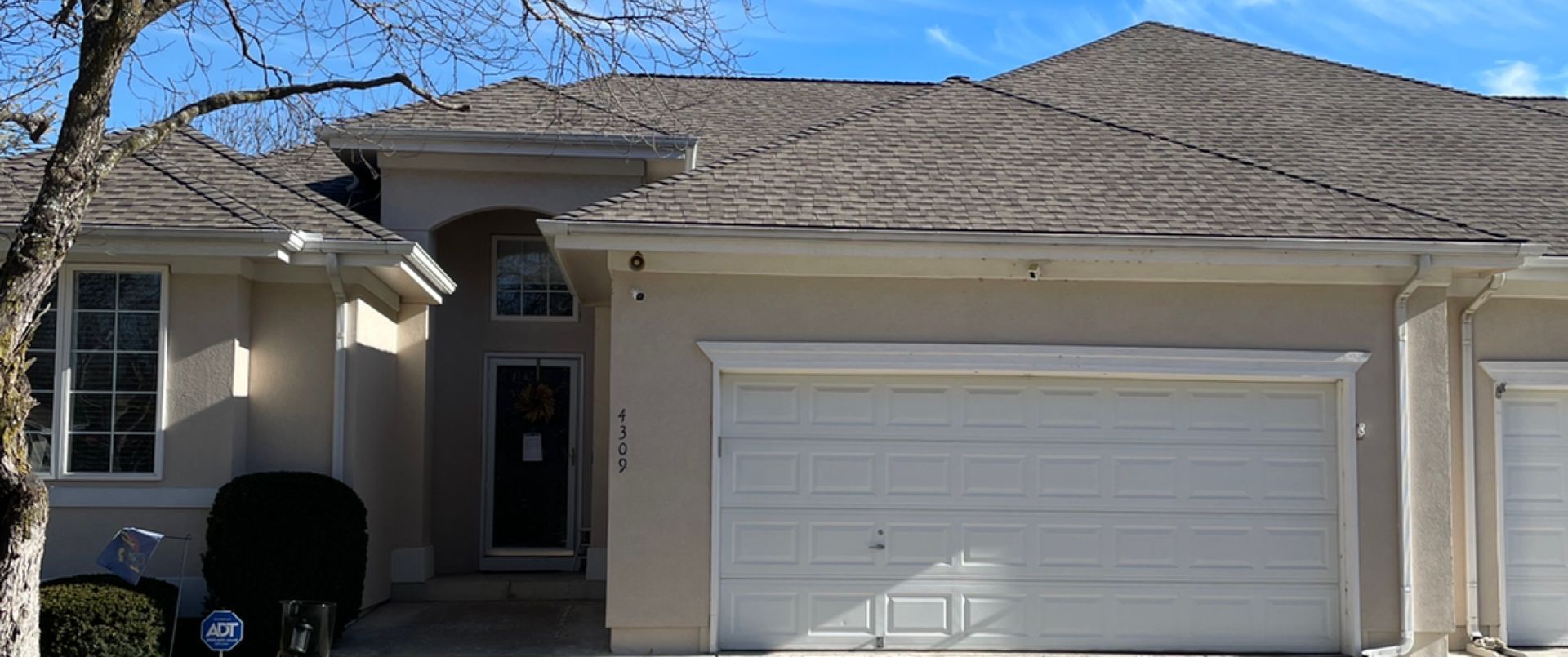 Suburban house exterior with beige siding, attached two-car garage, and front entry under a cloudy sky