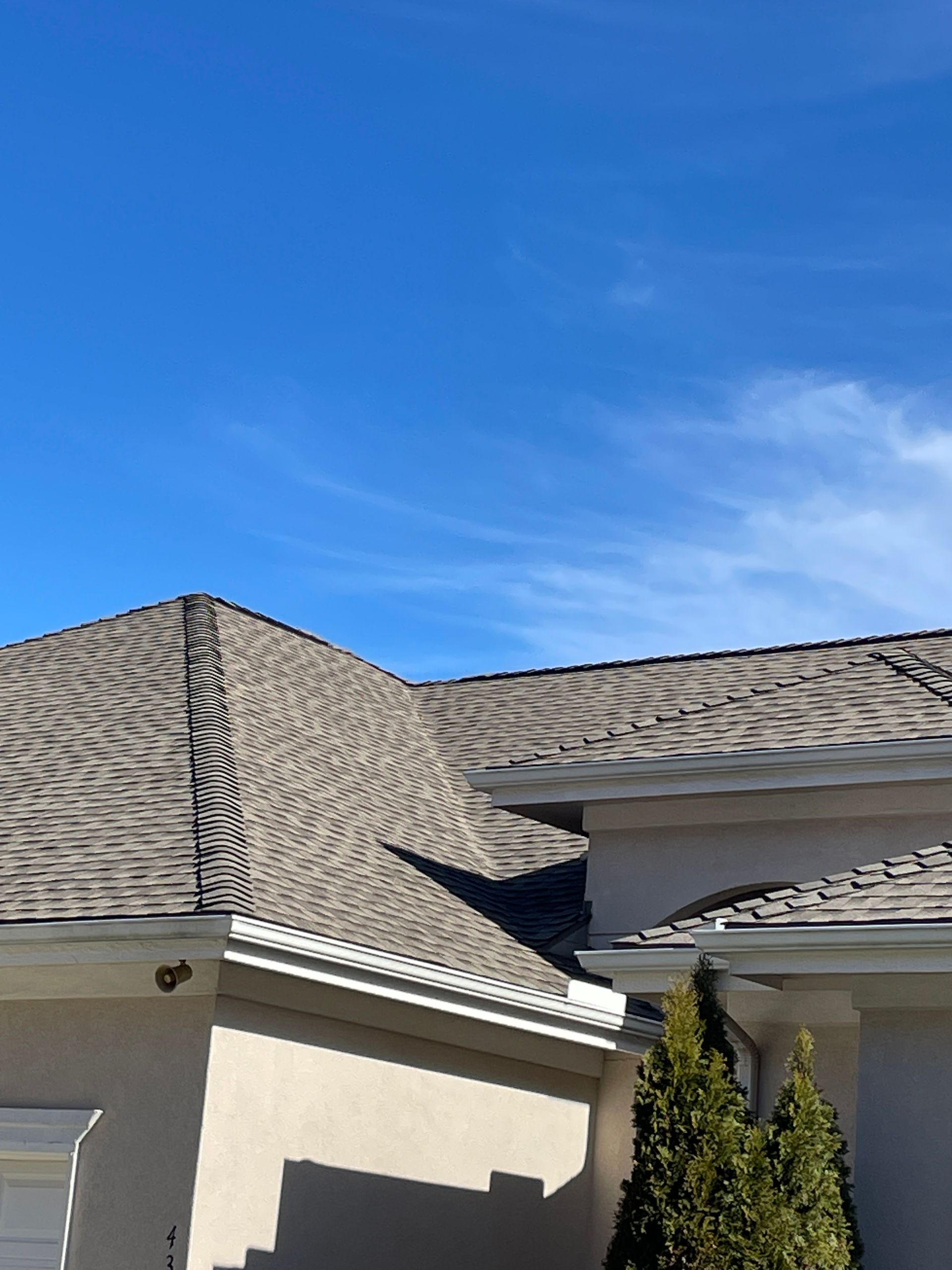 Close-up of a beige house roof with gray shingles against a bright blue sky