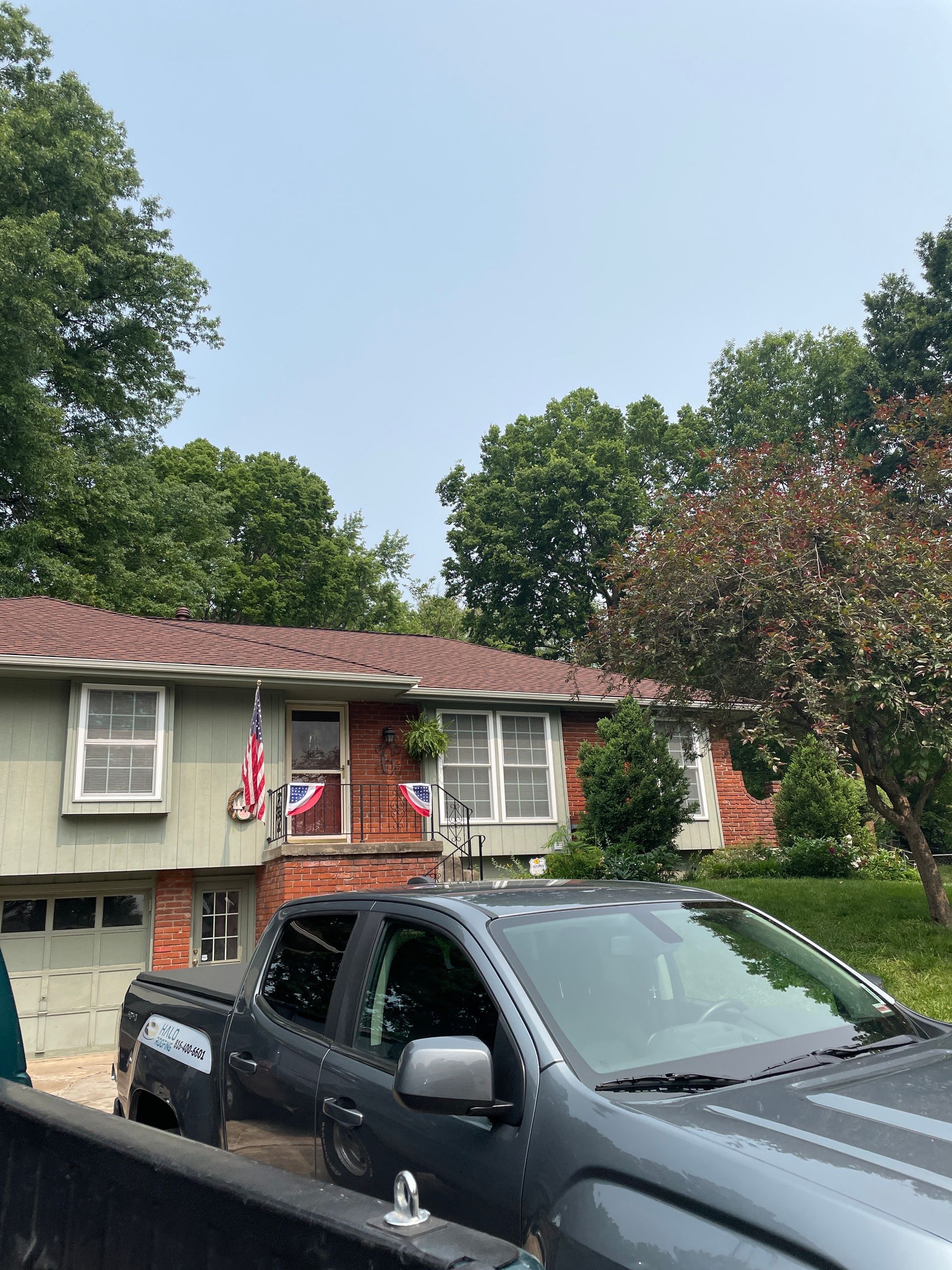 House with American flag and black pickup truck parked in front yard under trees