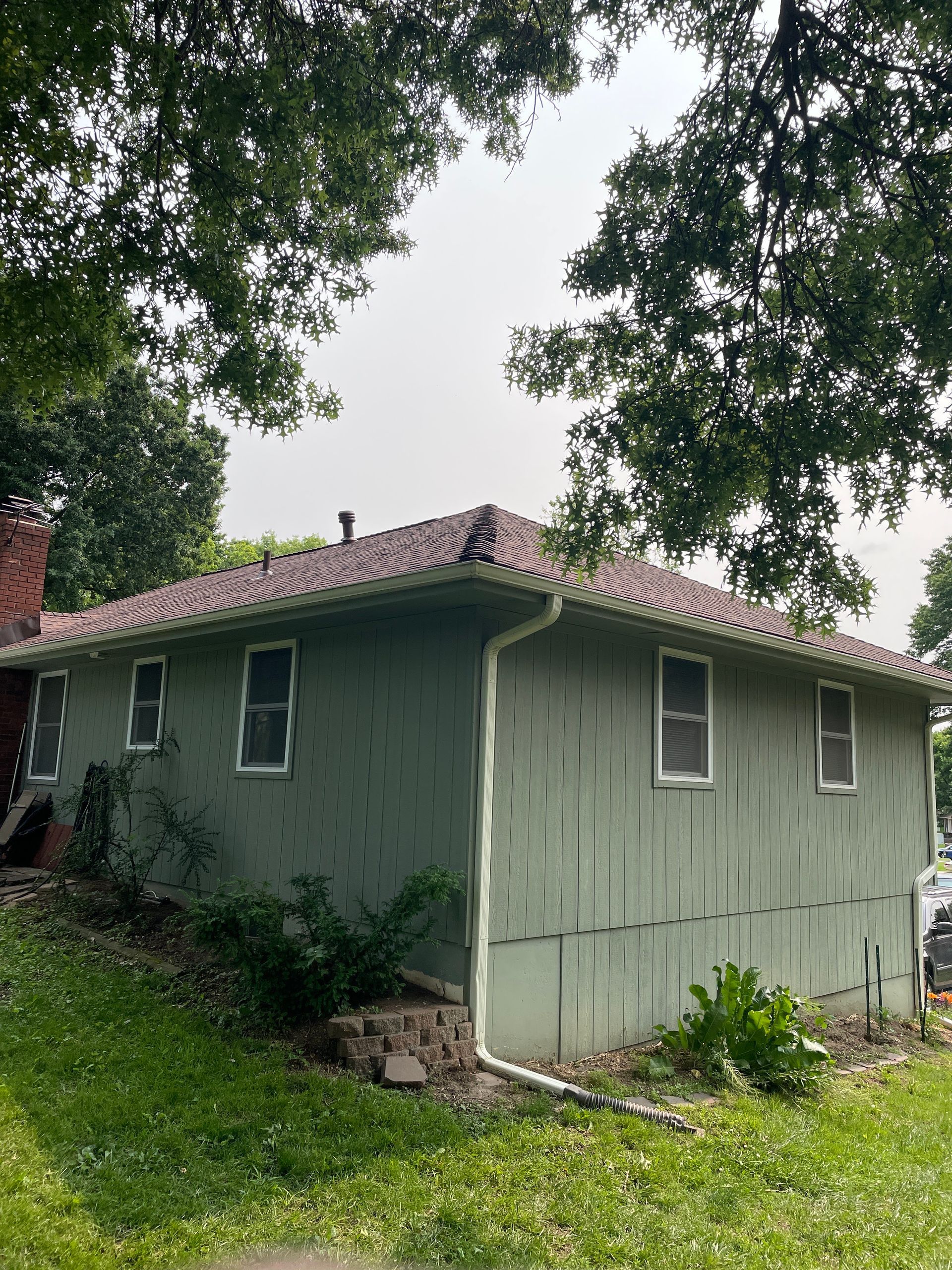 Small green house with a red-tiled roof, viewed from the side under leafy trees.