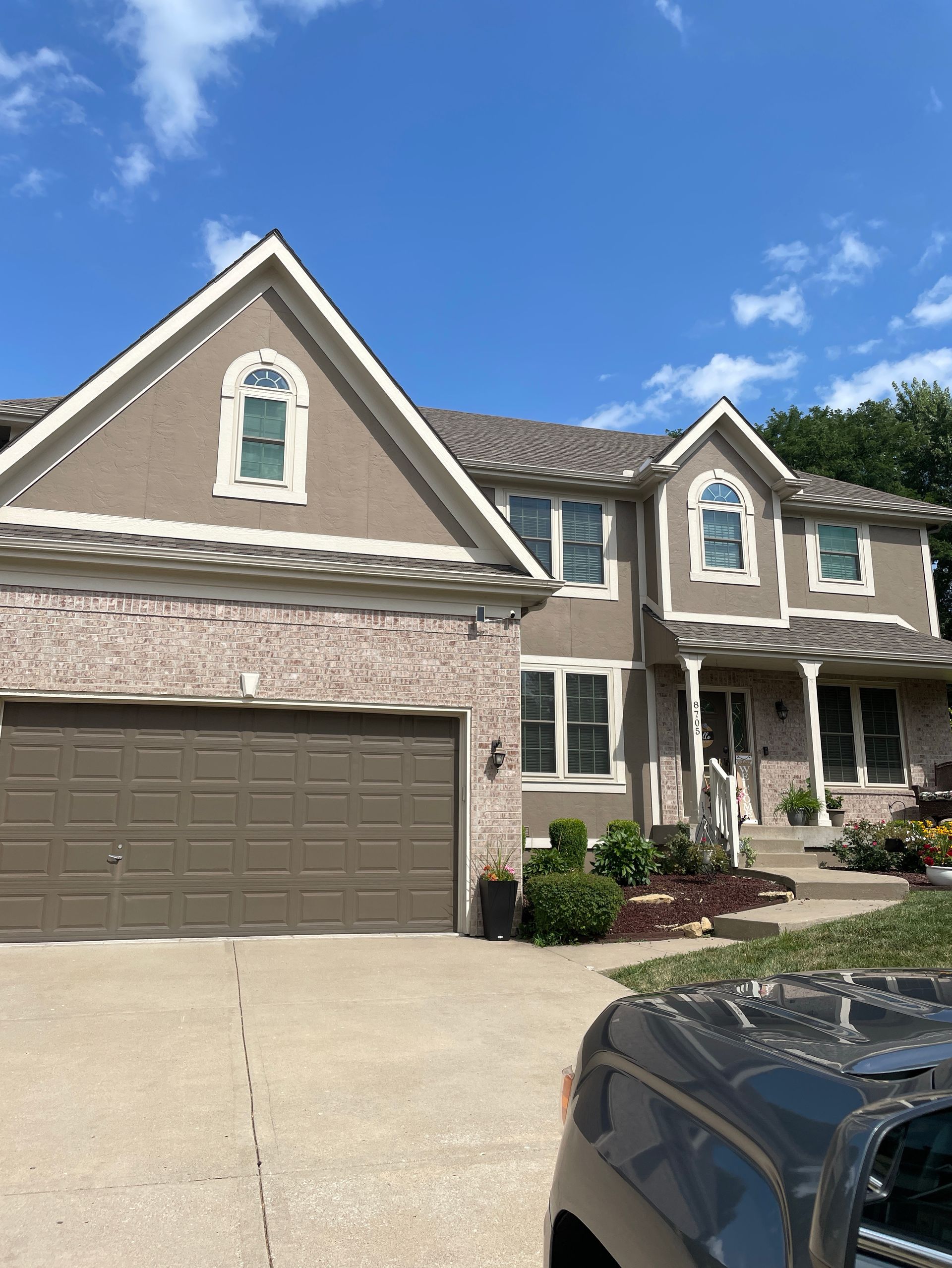 Two-story suburban house with stone facade, brown garage, and front porch under a blue sky