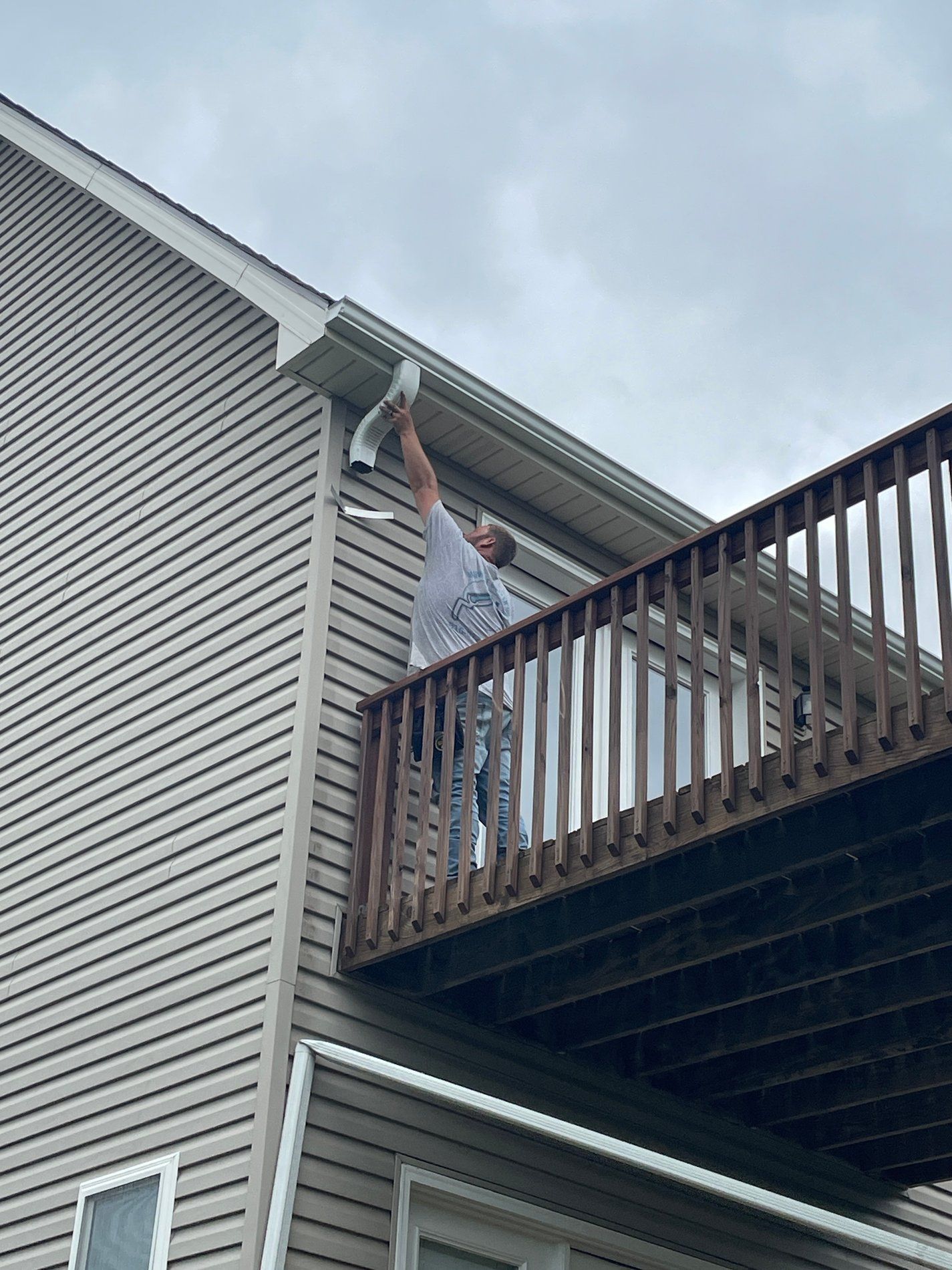 Person on a wooden balcony reaching up to adjust a light fixture on a house exterior.
