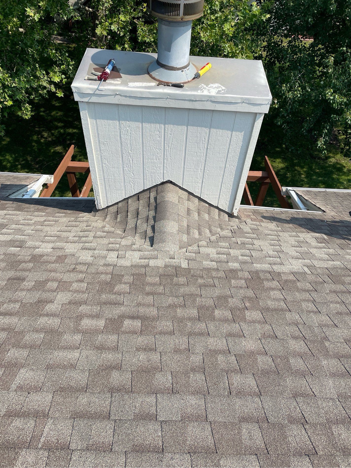 Roof shingles leading to a white chimney with metal vent and small tools on top, viewed from above