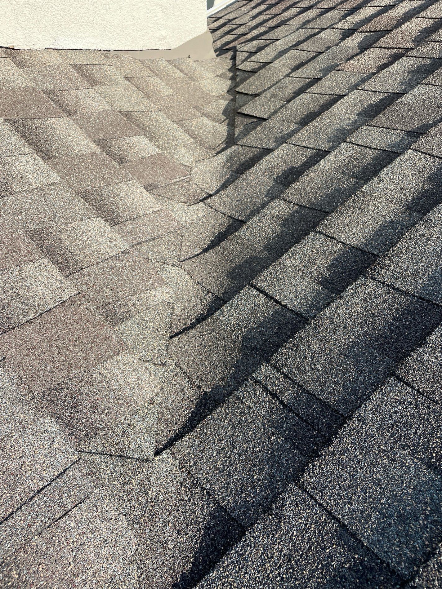 Close-up of gray asphalt roof shingles with visible ridges and texture in sunlight