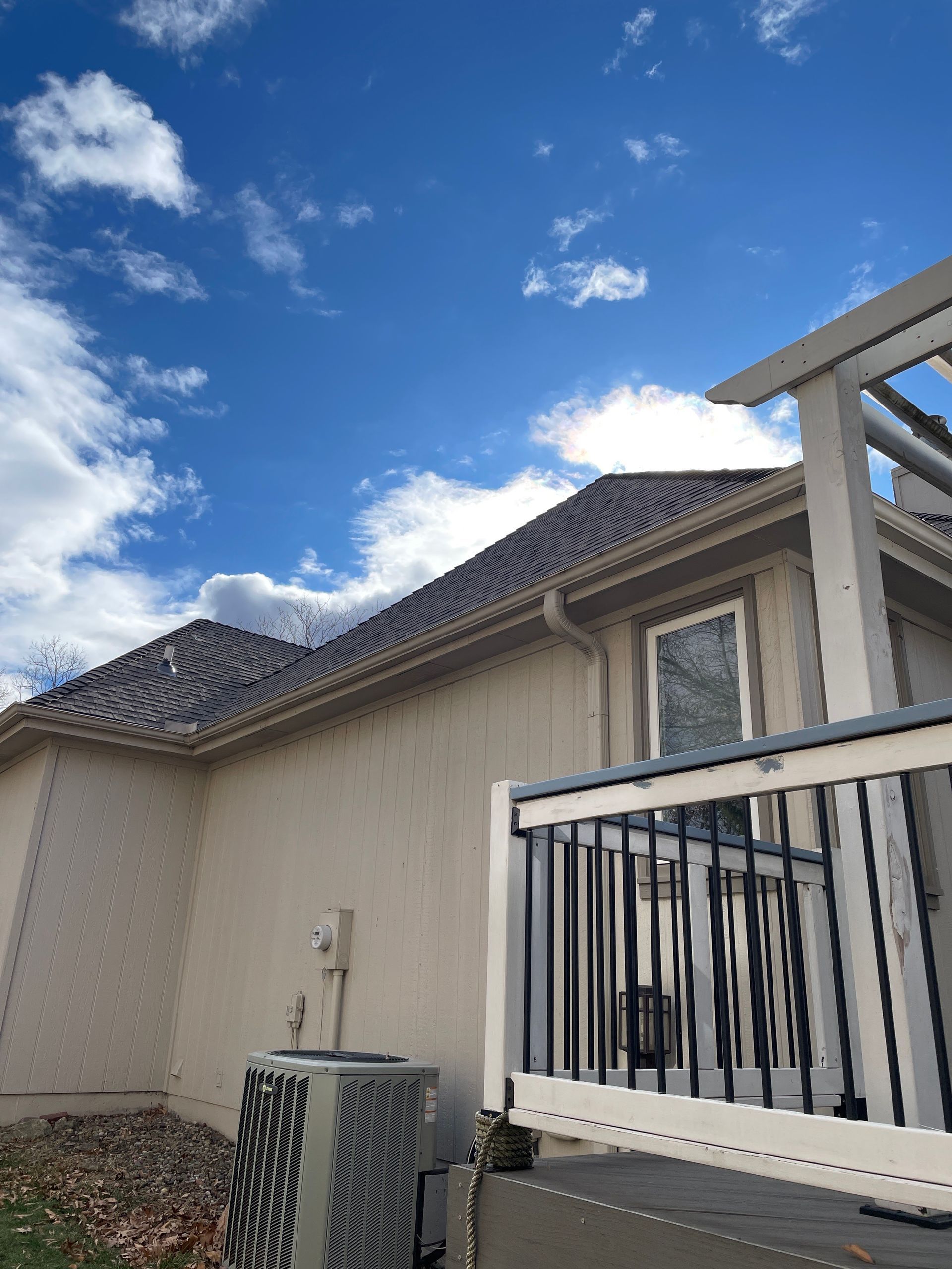 House exterior with beige siding, tiled roof, white balcony railing, and blue sky with clouds