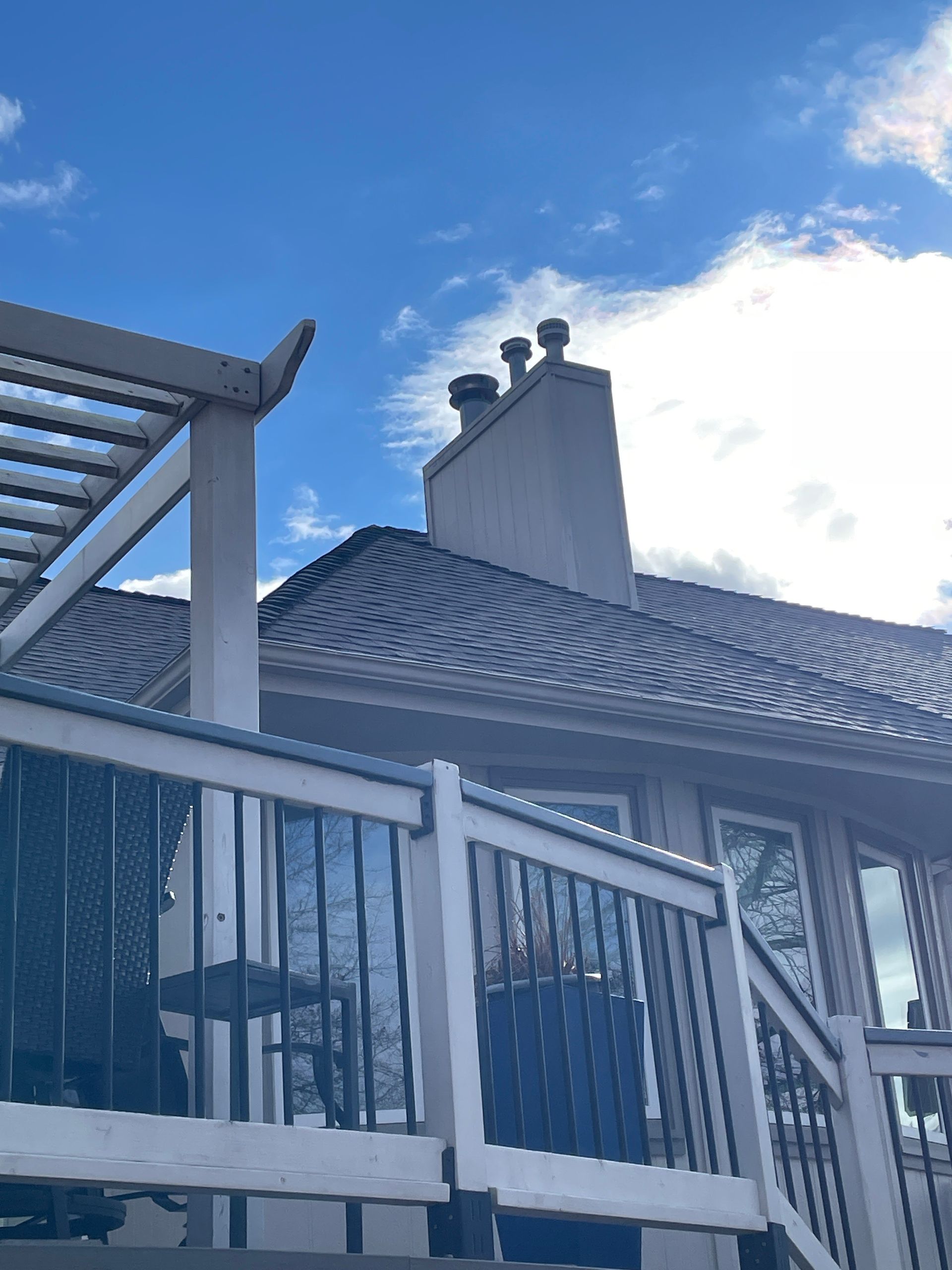 Blue house exterior with sloped roof, white trim, and a deck railing under a bright sky