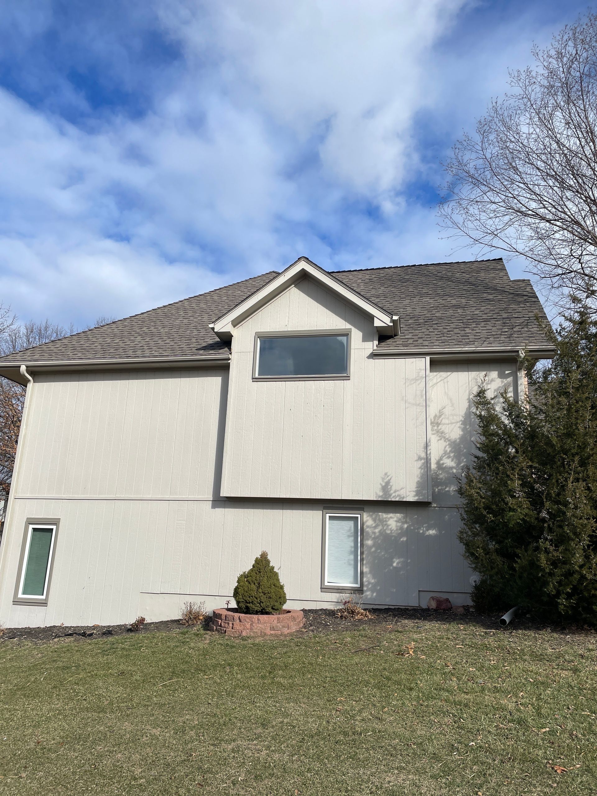Two-story beige house with a tiled roof and small windows under a blue, cloudy sky