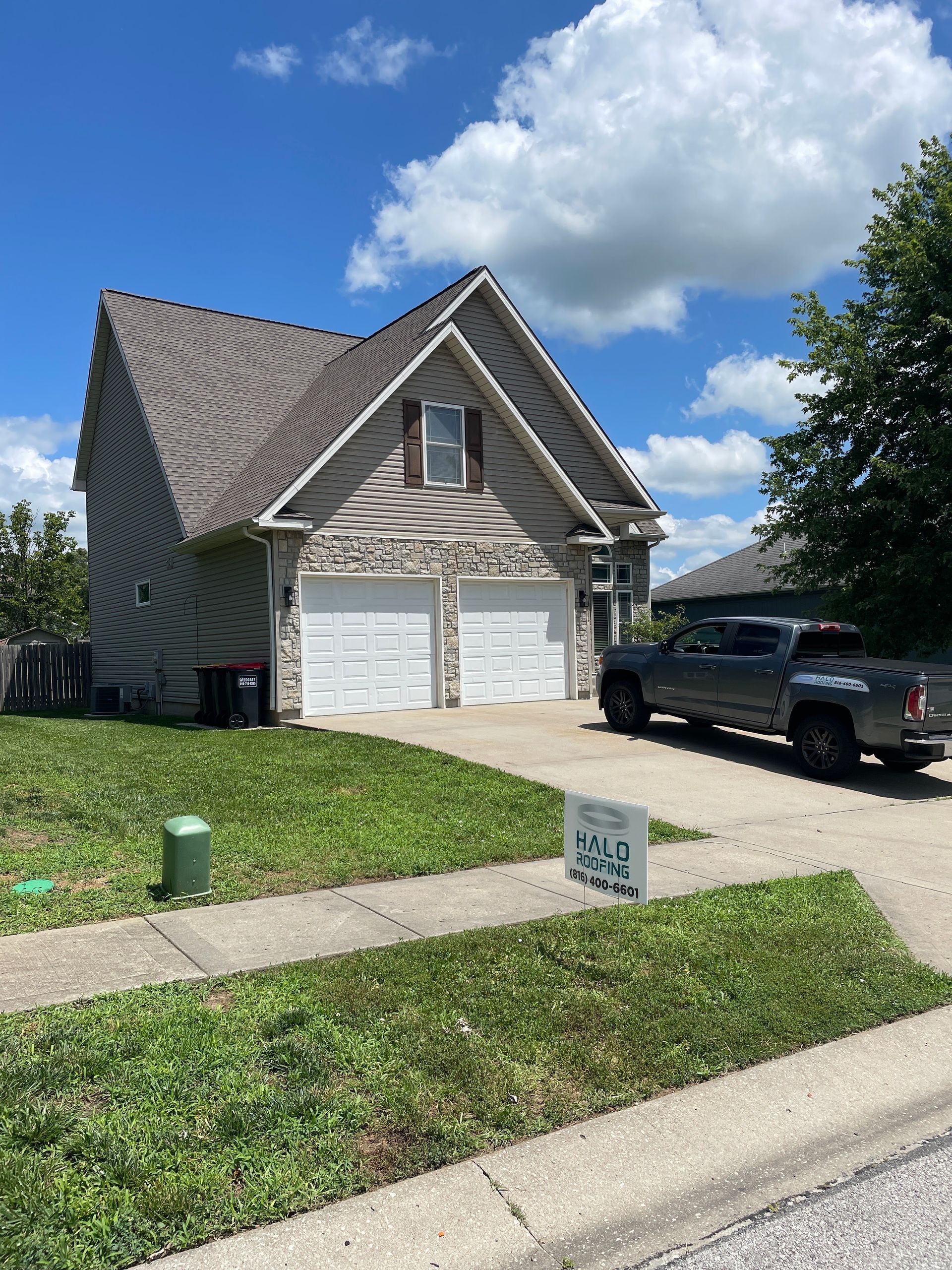 Suburban house with steep roof, white garage doors, black truck, and a lawn under a blue sky