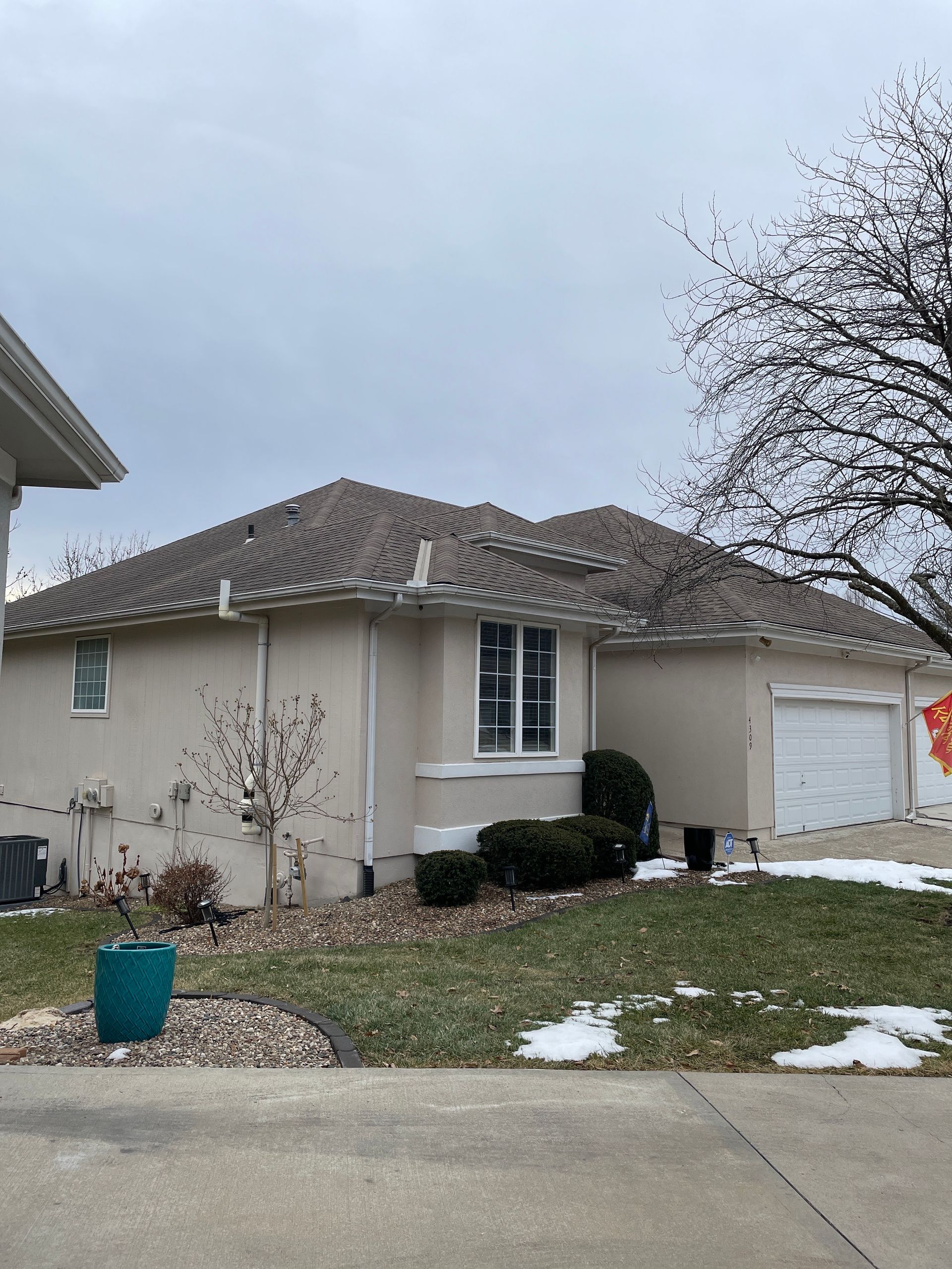 Single-story beige house with a tiled roof, white garage, and a small snowy front yard under an overcast sky
