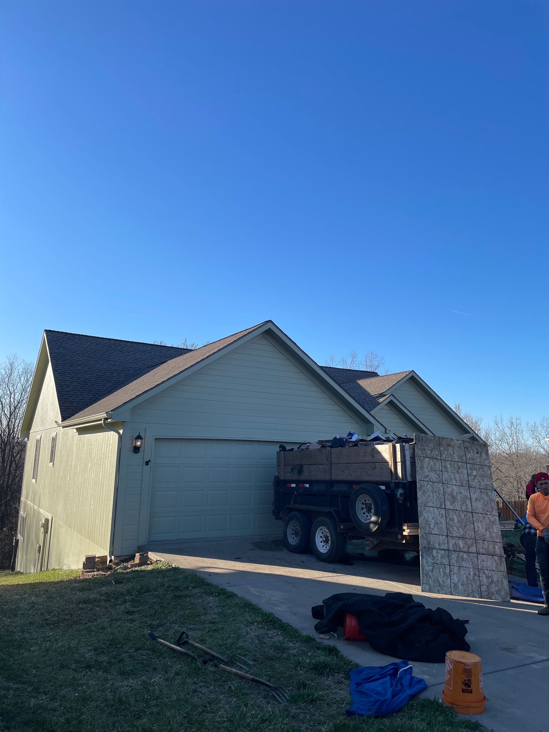 Suburban house with open garage, blue sky, and construction materials in the driveway