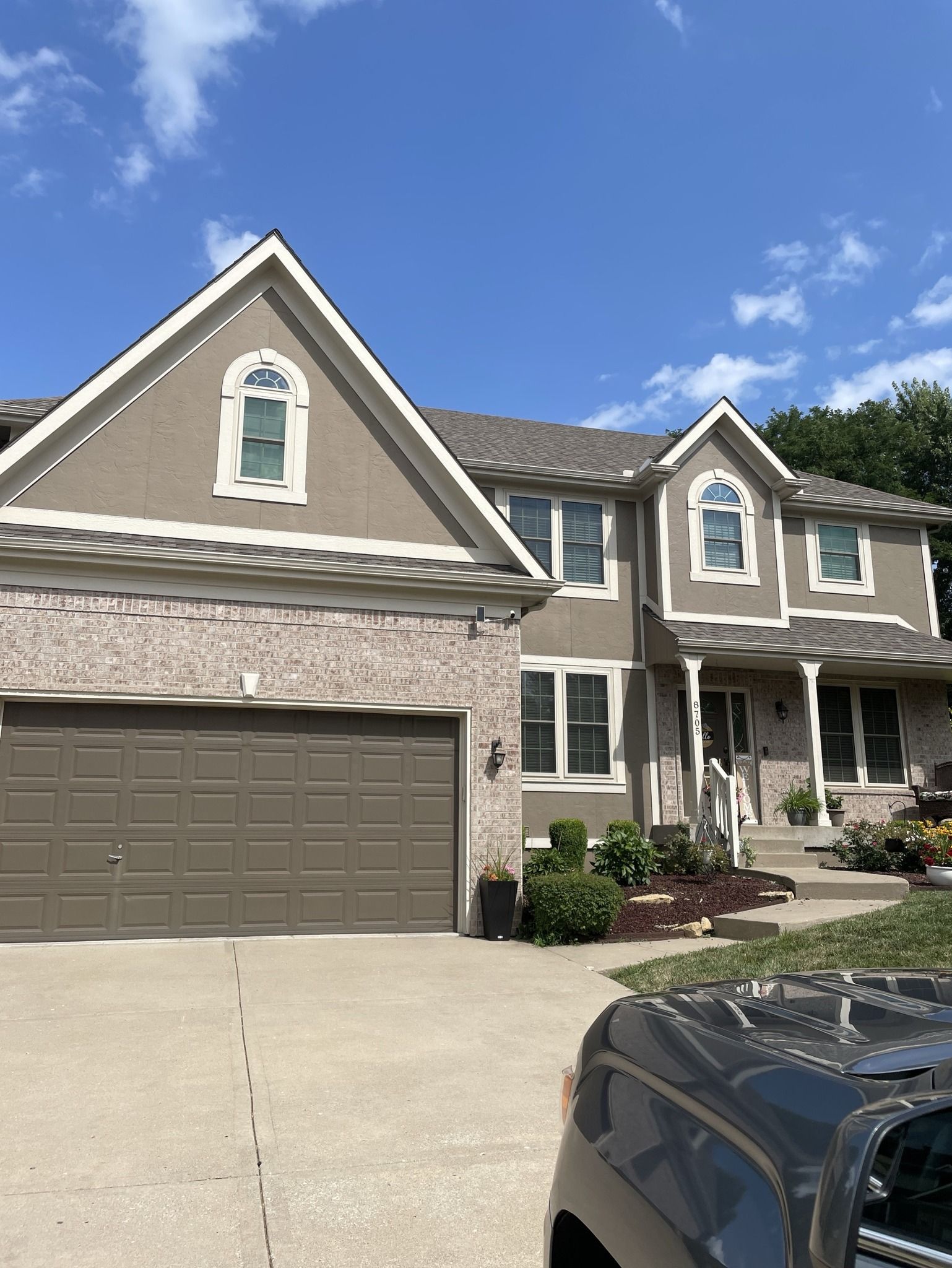 Suburban two-story house with stone facade, attached garage, and a car in the driveway under a blue sky