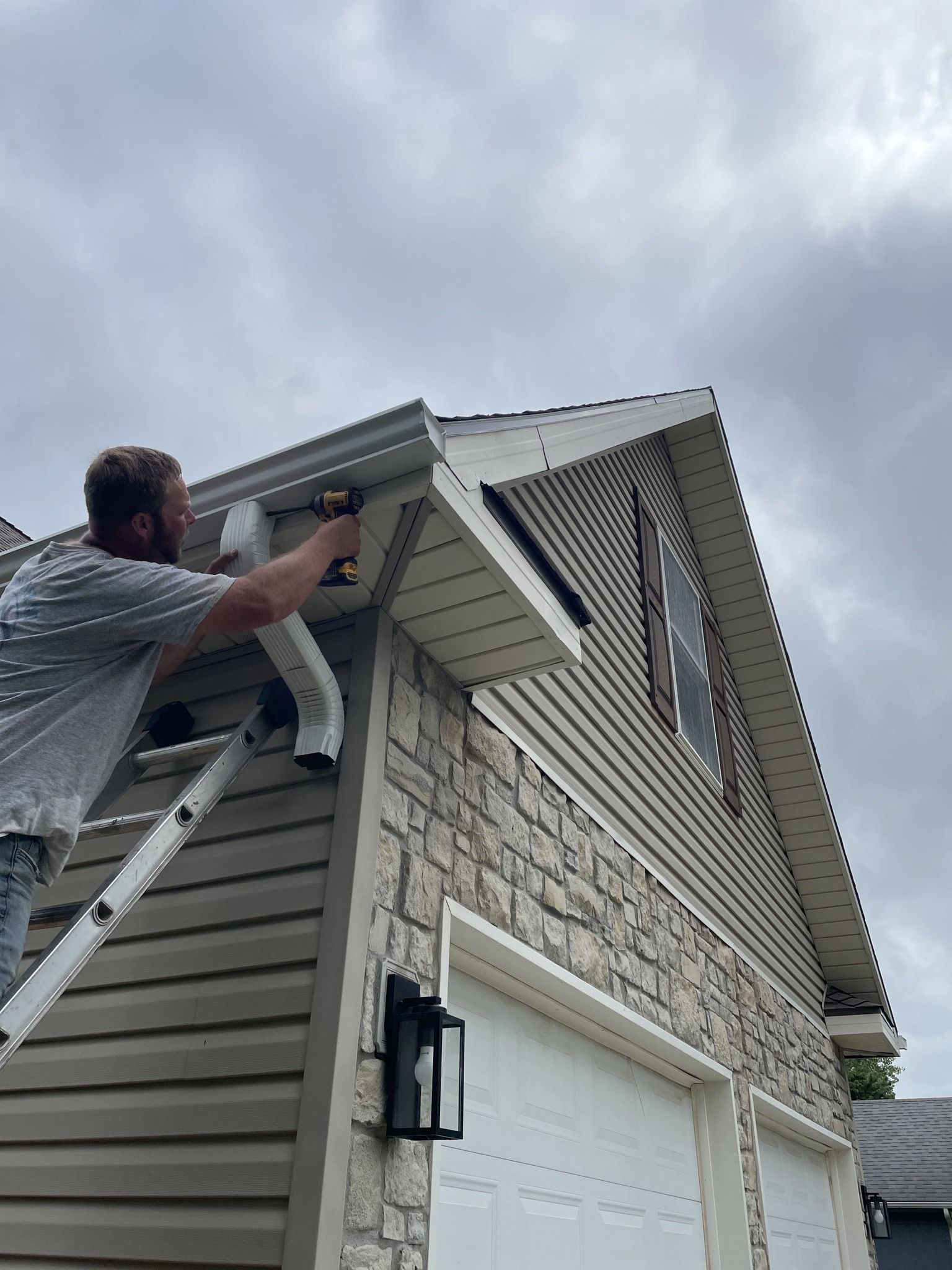 Worker on a ladder painting a house’s white trim under a cloudy sky