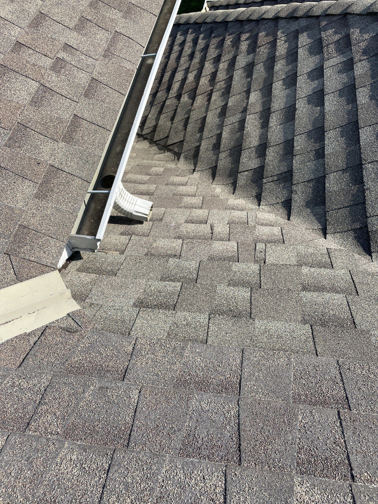 Gray shingled roof with a white gutter and downspout beside a darker roof section