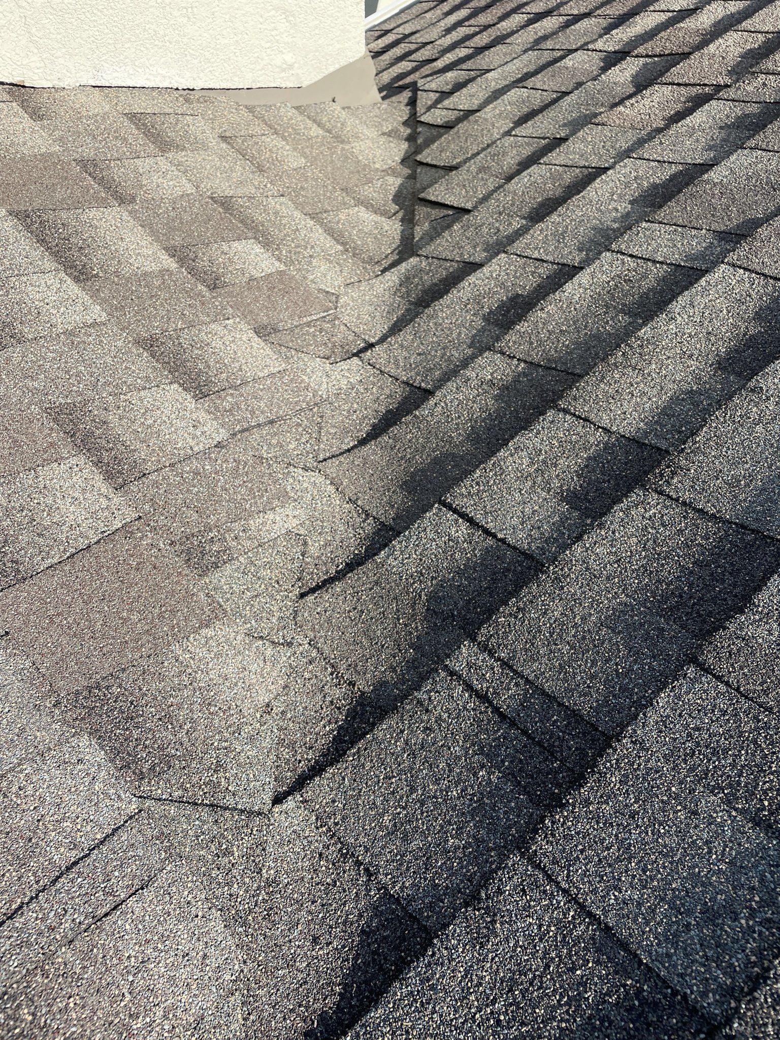 Close-up of gray asphalt roof shingles with diagonal sunlight and shadow patterns