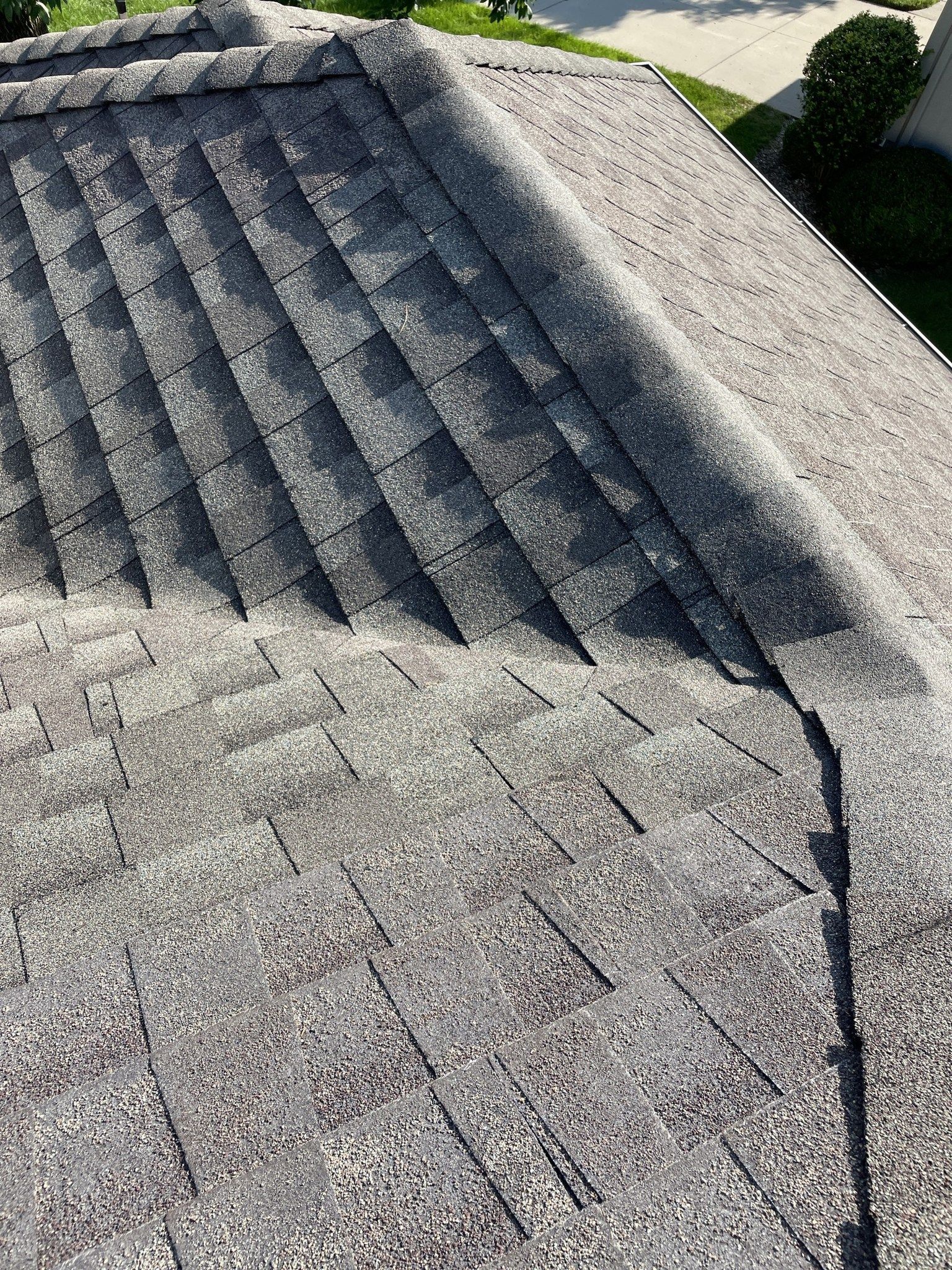 Gray shingled roof with a dark ridge and textured asphalt surface, viewed from above