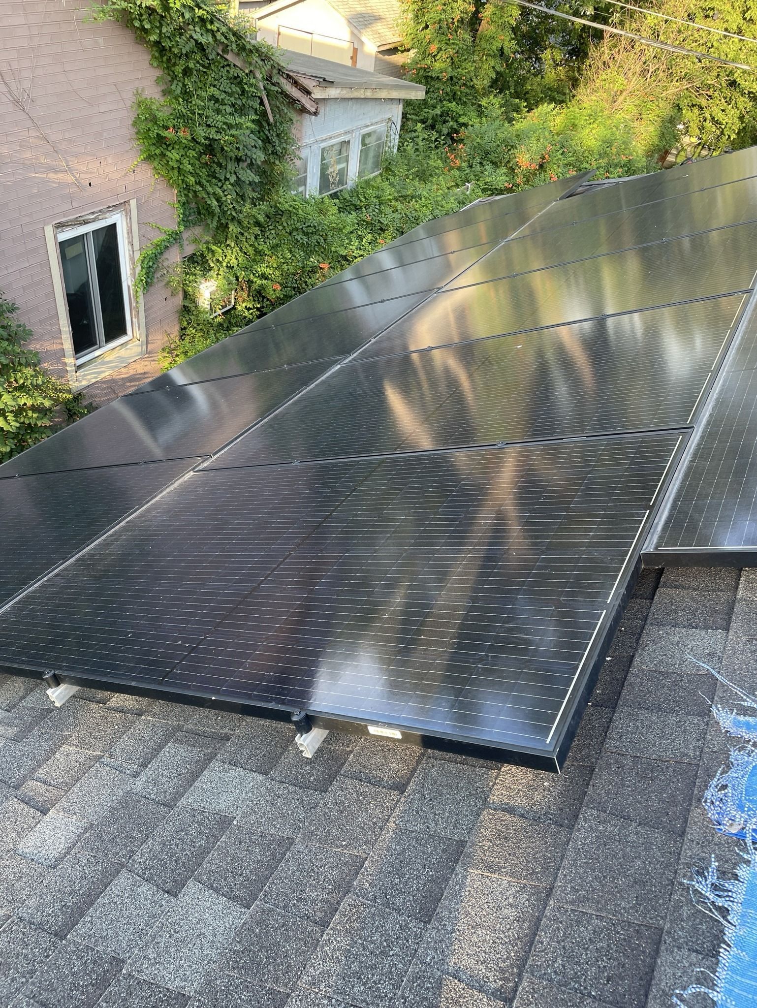 Solar panels installed on a sloped roof beside a brick house and greenery.