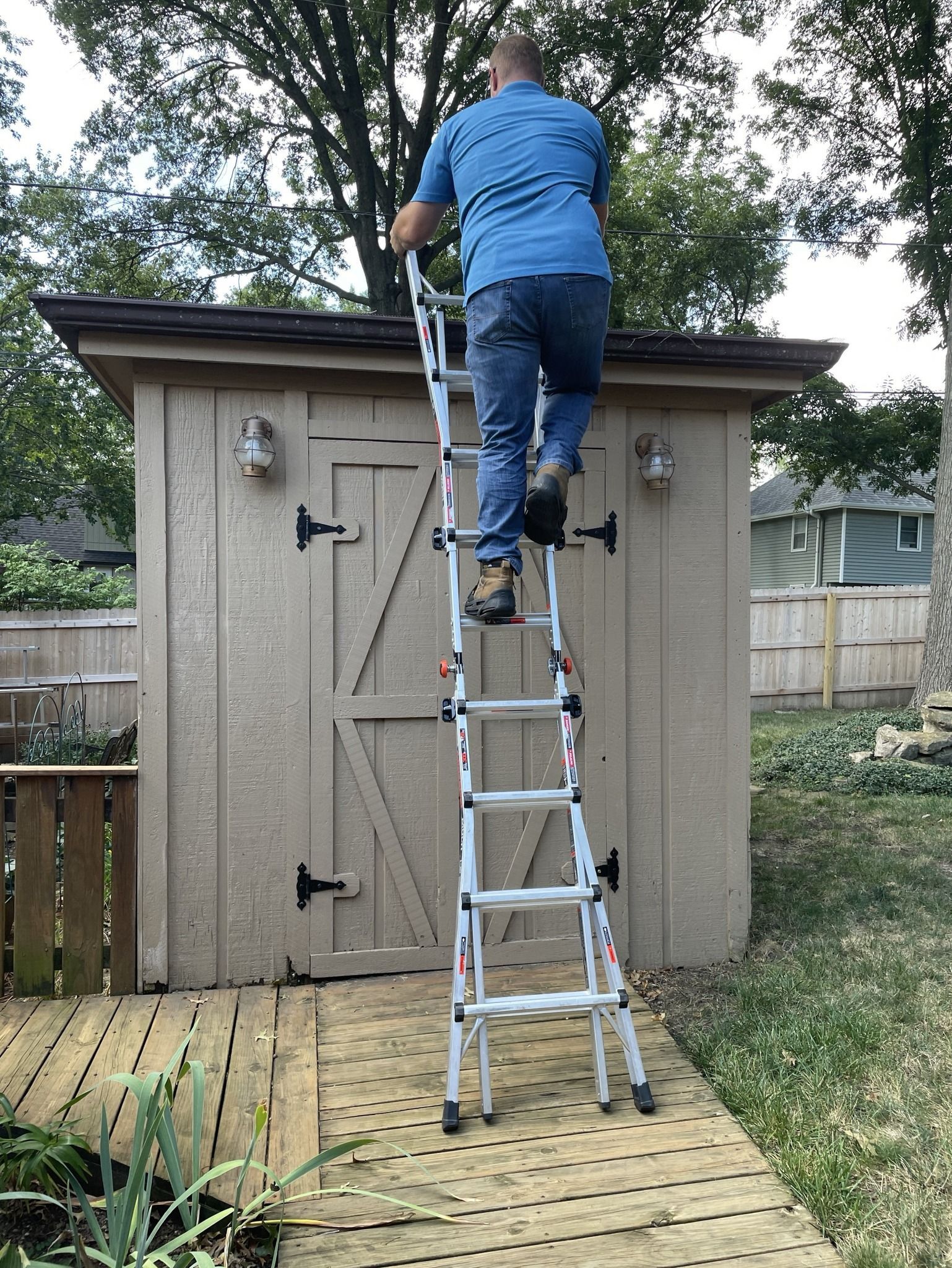 Person on a ladder cleaning a shed roof in a backyard