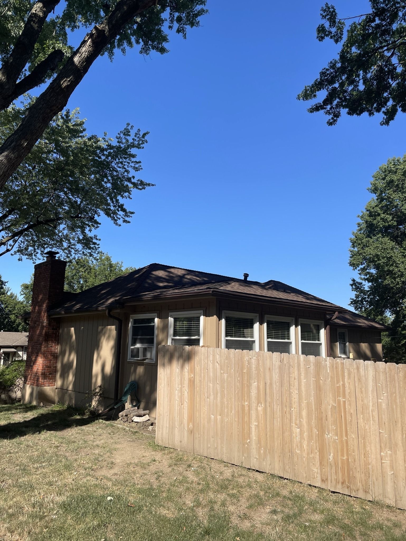 Single-story house with tan roof and wooden fence under a bright blue sky.