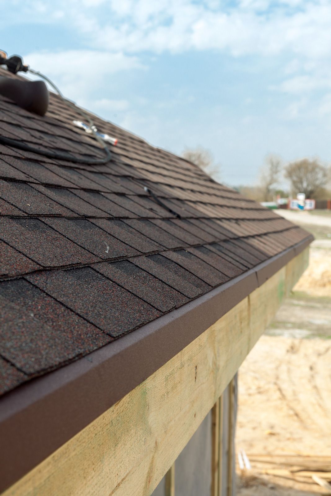 Close-up of brown shingle roof edge on a beige building under a blue sky