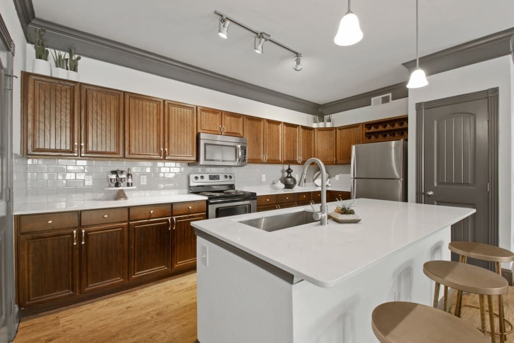 a kitchen with wooden cabinets, stainless steel appliances, a sink, and a refrigerator at Marquis on Evans in San Antonio, TX.