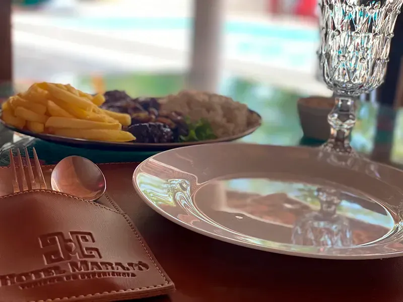 Uma refeição com batatas fritas, arroz e carne num prato, ao lado de um prato vazio, talheres e um copo, numa mesa do Hotel Mataro.
