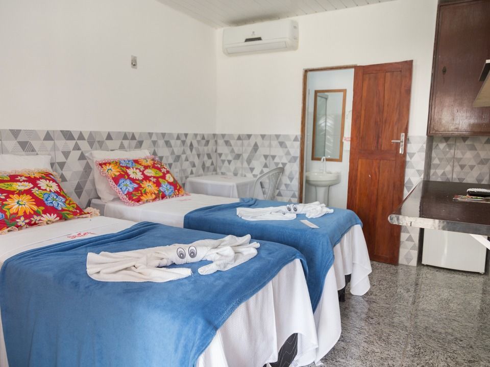Um quarto de hotel com duas camas de solteiro, almofadas florais, mantas azuis, toalhas dobradas em formato de origami, paredes estampadas e um banheiro.