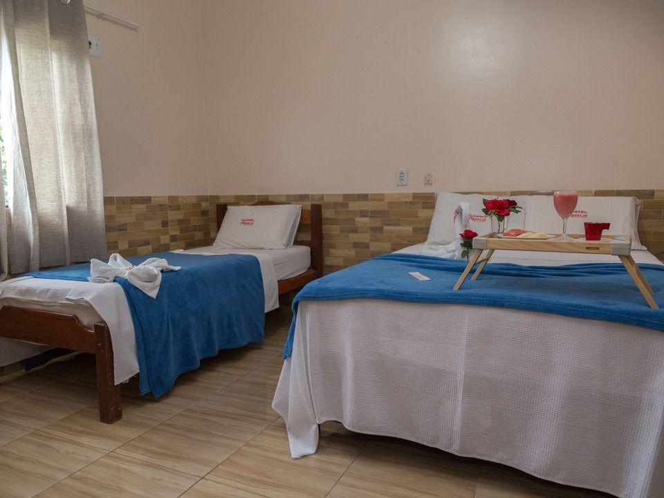 Um quarto de hotel com duas camas, cobertores azuis e uma bandeja de café da manhã na cama maior, encostada em uma parede de azulejos.