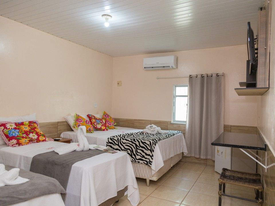 Um quarto de hotel com duas camas, uma com almofadas florais e a outra com uma manta de estampa de zebra, perto de uma janela e uma TV fixada na parede.