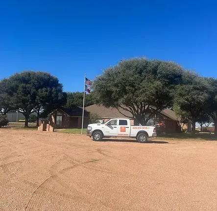 A white truck is parked in a dirt lot in front of a house.