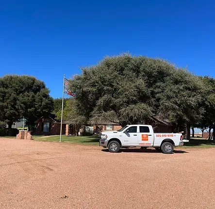 A white truck is parked in a gravel lot in front of a house.