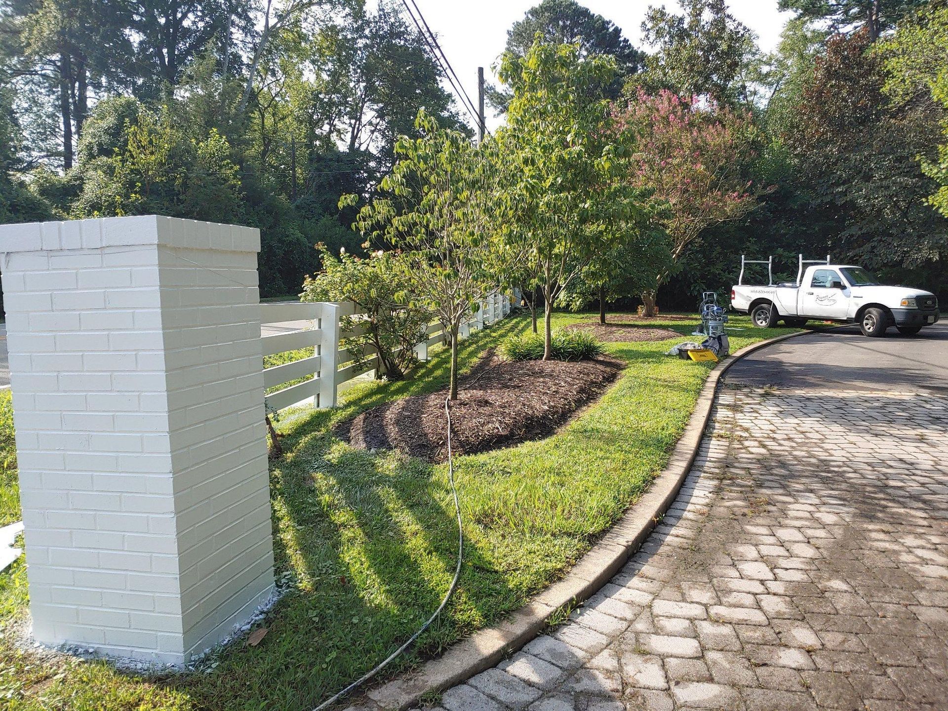 A white truck is parked in a driveway next to a white brick pillar.