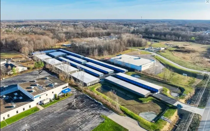 Aerial view of an industrial warehouse complex with long blue-roofed buildings and surrounding roads.