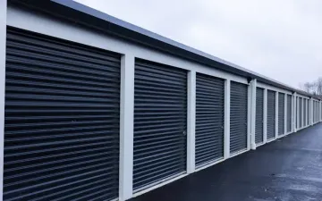 Row of dark storage unit doors along a white building beside a paved drive