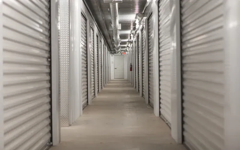 Long corridor in a storage facility with rows of closed metal unit doors on both sides.