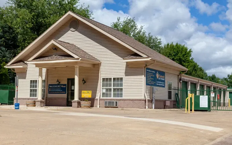 Small tan and brown building with covered entrance and green doors on a sunny day