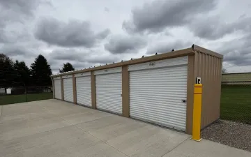 Row of white storage unit garage doors beside a concrete lot under cloudy skies