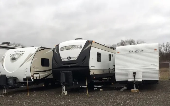 Three RV trailers parked side by side in a lot under a cloudy sky