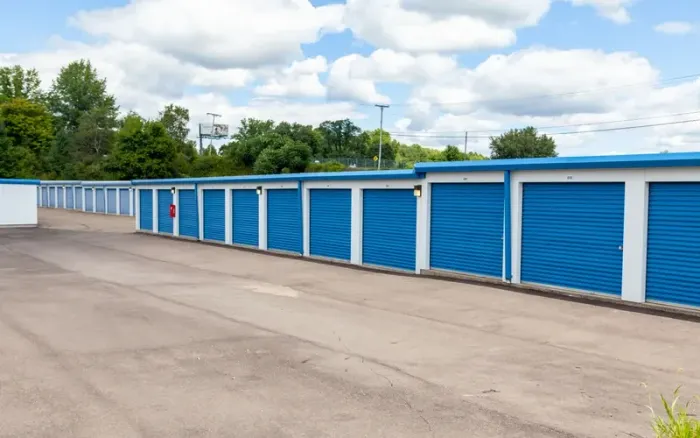 Row of blue storage unit doors beside an empty paved lot under a cloudy sky