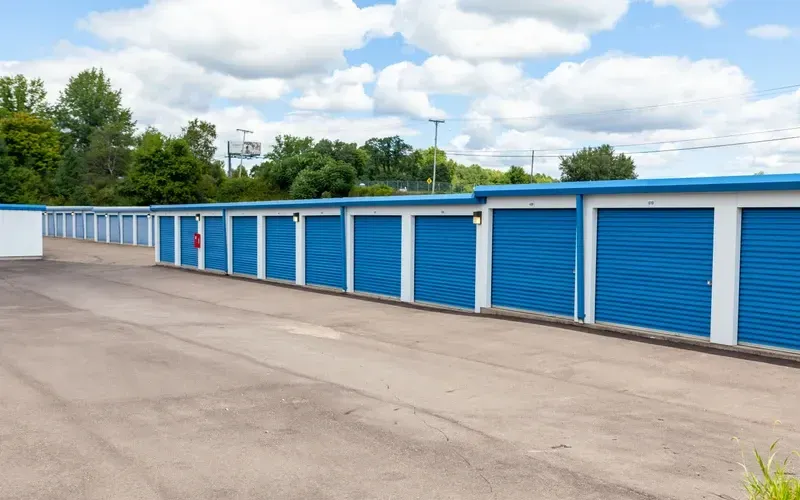 Row of blue and white storage unit doors along a gravel drive under a partly cloudy sky