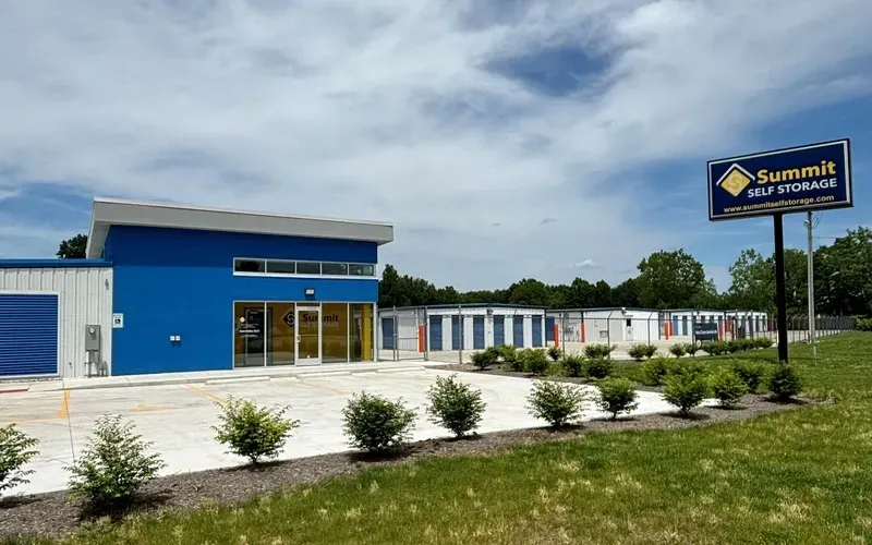 Blue self-storage building with white units and a roadside sign under a cloudy sky