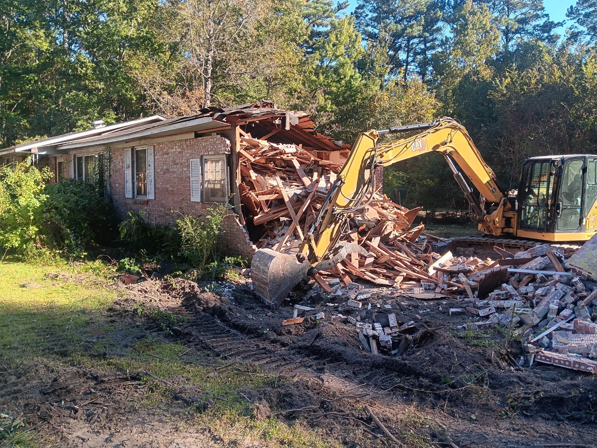 Yellow excavator demolishing a two-story building, creating dust and rubble.