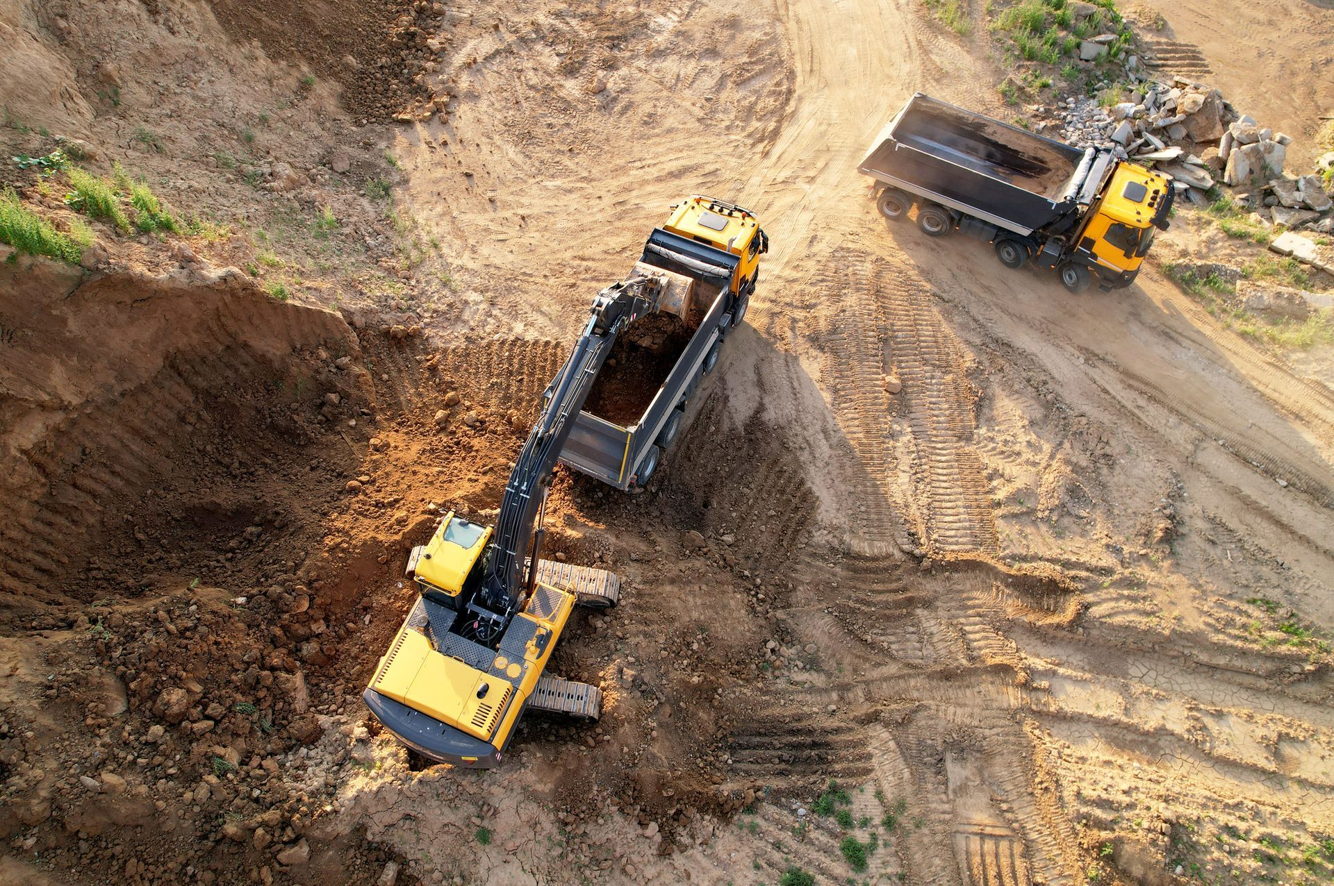 Excavator loading a dump truck at a construction site; brown earth, yellow machinery, top-down view.